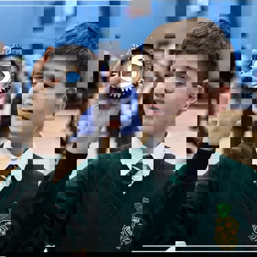 Young person in a school hall holding a piece of scientific equipment as other young people in the background work