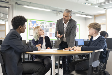 Three young people sit around a table in a school classroom as a teacher or careers adviser talks to them 
