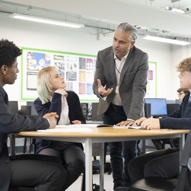 Three young people sit around a table in a school classroom as a teacher or careers adviser talks to them