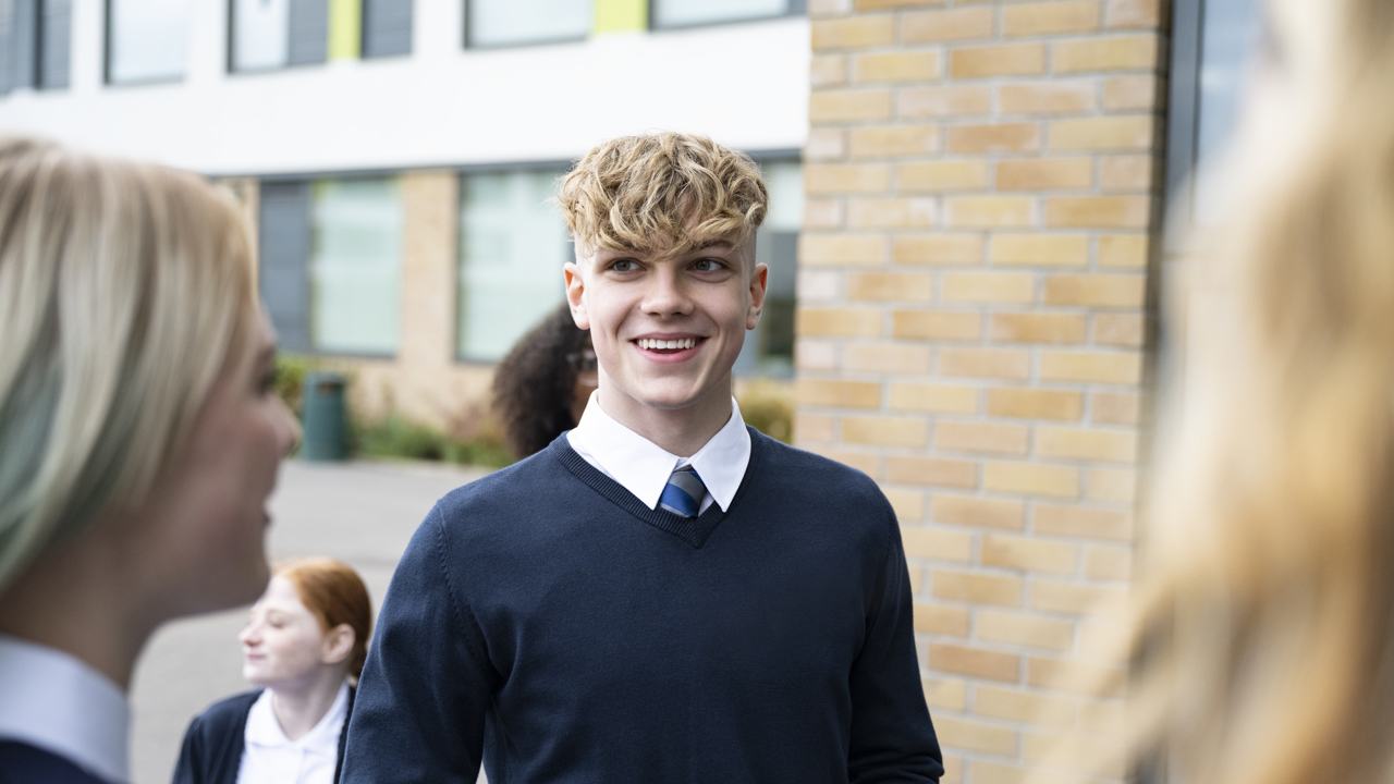 A group of young people smiling outside their school building