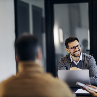 A group of people at work sit around a meeting table talking