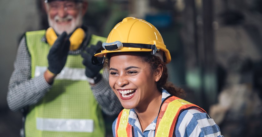Young woman in PPE laughing while older supervisors laughs and applauds behind her
