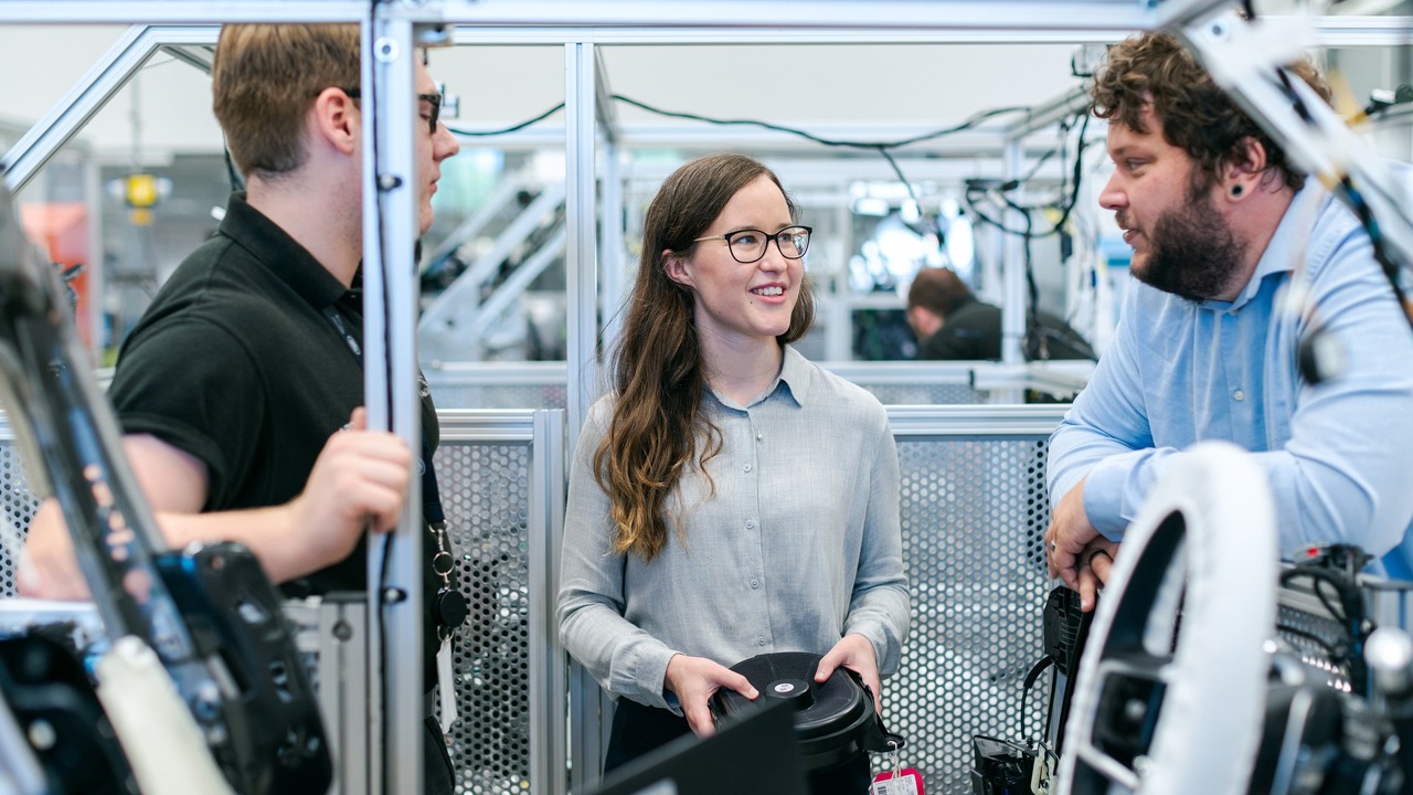 Two male and one female manufacturing engineers in the workshop discussing their work