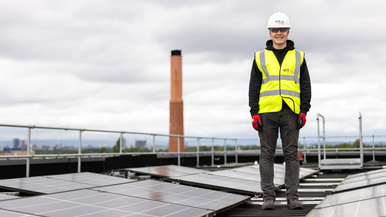 Apprentice solar panel engineer standing on a roof containing numerous solar panels