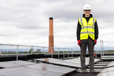 Apprentice solar panel engineer standing on a roof containing numerous solar panels