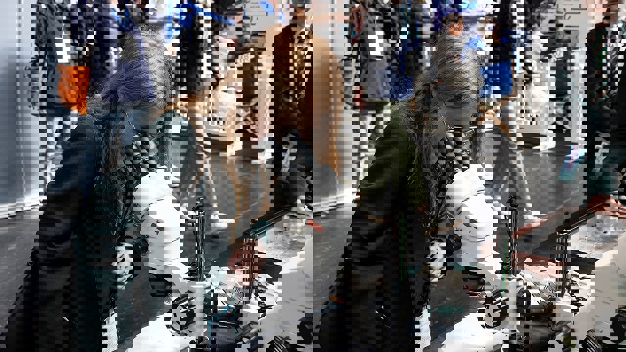 A young person at The Big Bang Fair looks into a microscope as others in the background walk by