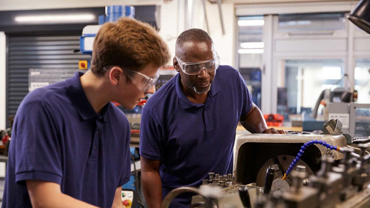 Two engineers in a workshop operating machinery they are wearing protective clothing