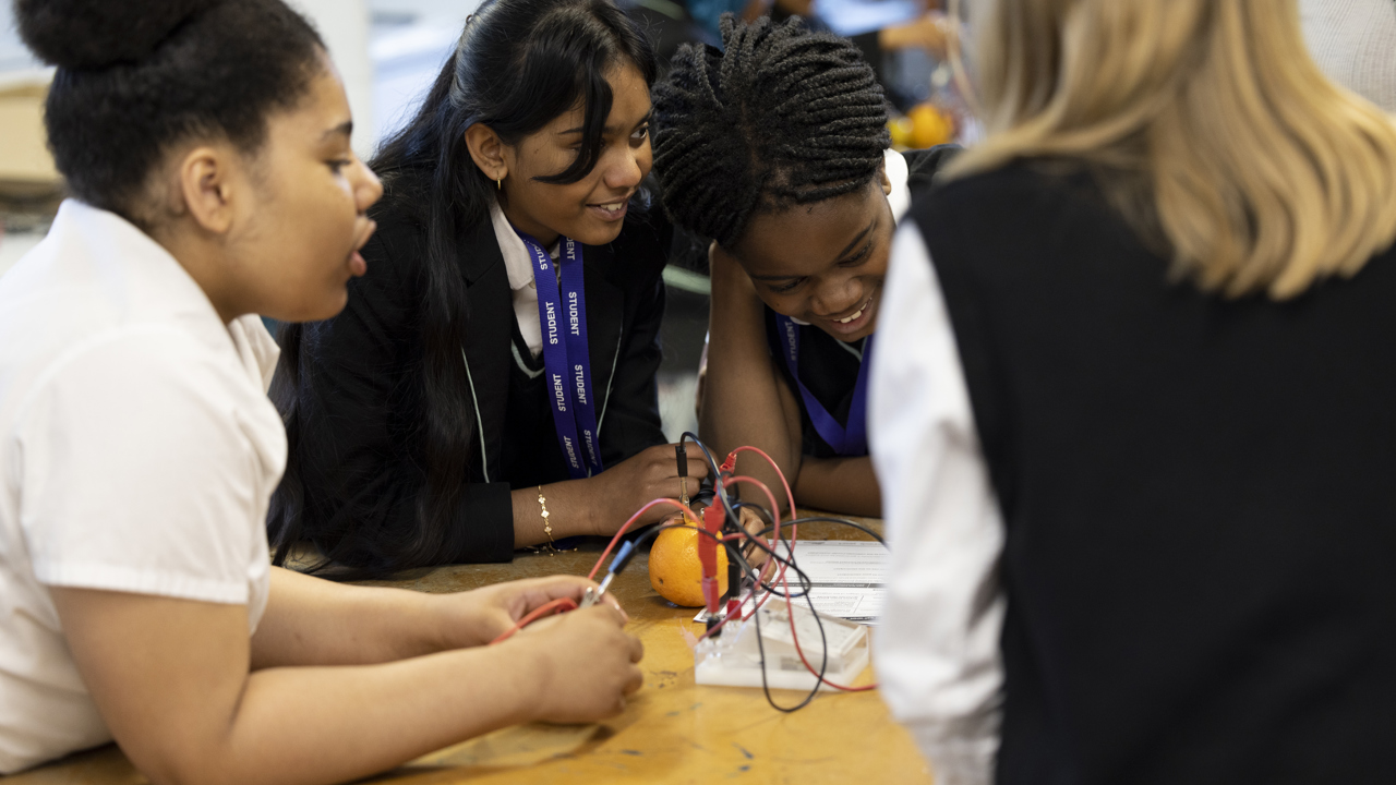 A group of girls in a school science lab smiling as they work at the bench. They are conducting a science experiment. 