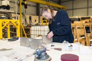 A T Level student wearing protective goggles at a work bench in a warehouse, constructing using metal pieces