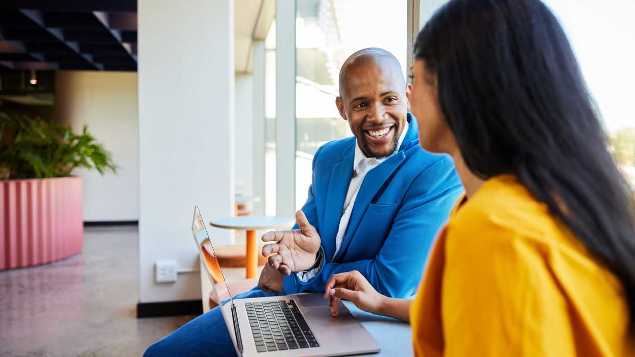 Two people at work in a relaxed meeting looking at a laptop and smiling 