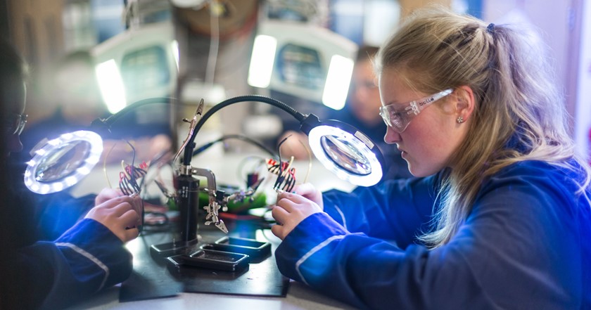 A young female engineer examines electronics through magnifying lens