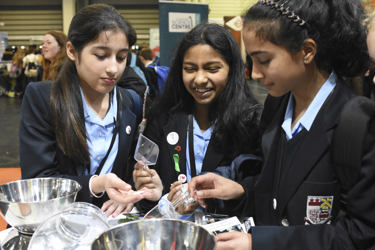 Three young people interact with exhibits and stands and activities at The Big Bang Fair