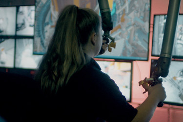A person operates machinery while watching screens
