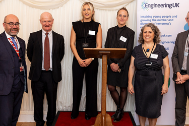 A group of professionals stand on a stage with a lectern facing the camera smiling