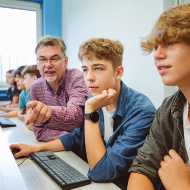 A group of students and their teacher in a school computer lab looking at screens