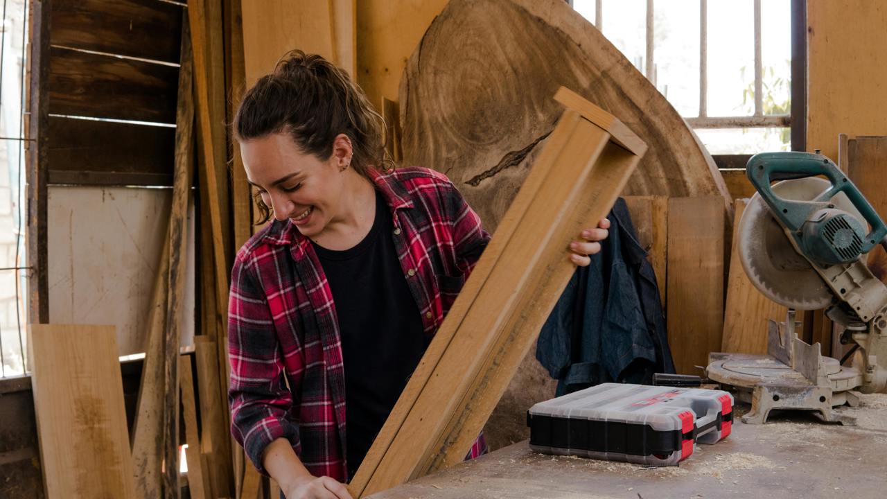 Someone in a workshop holding a piece of wood with equipment and toolbox around them